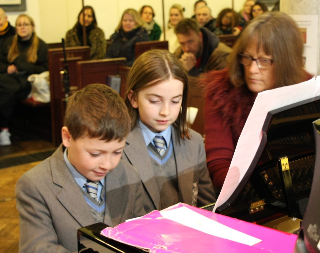 children playing the piano with their teacher