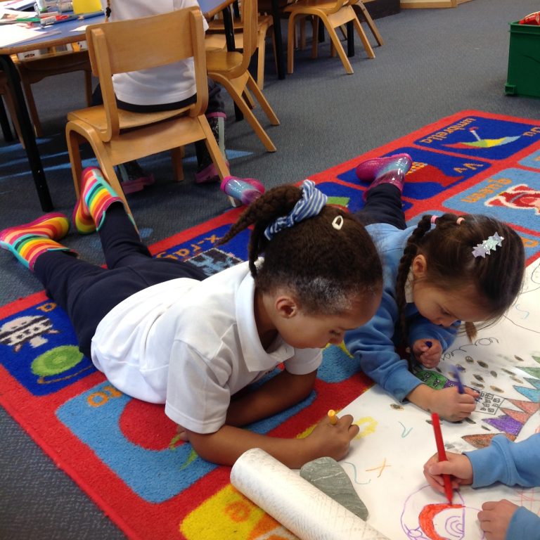 two girls lying on the floor to colour